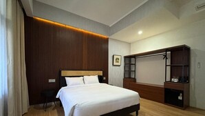 A hotel room with a bed, a desk, a chair, a wardrobe, and a wall-mounted TV. - And Living Hotel (Depok)