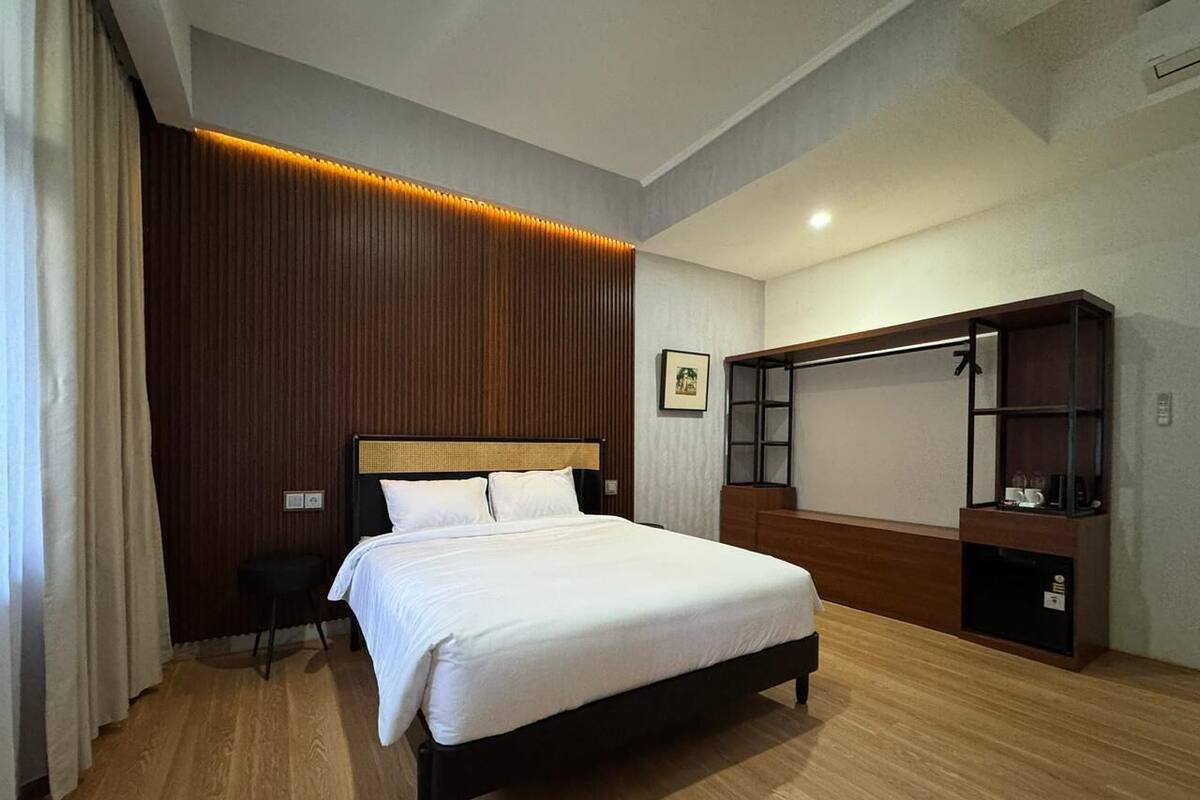 A hotel room with a bed, a desk, a chair, a wardrobe, and a wall-mounted TV.