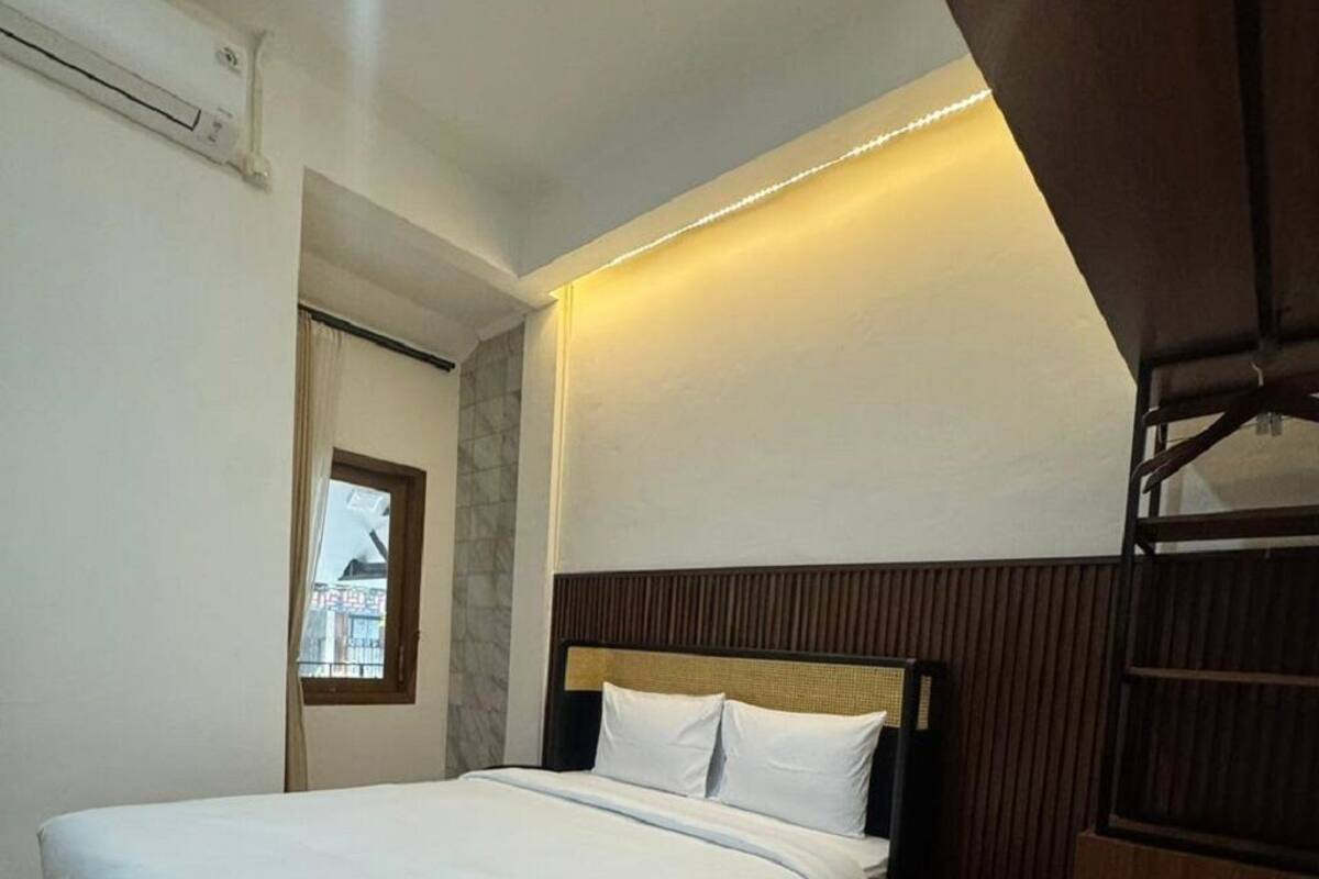 A modern bedroom with a bed, wooden headboard, and a small window.