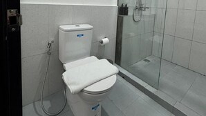 A bathroom with a toilet, a shower, and a towel rack. - And Living Hotel (Depok)