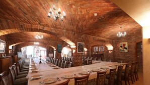 Une longue table à manger, dressée pour un repas, se trouve dans une pièce aux murs de briques et aux plafonds en arc de cercle.
