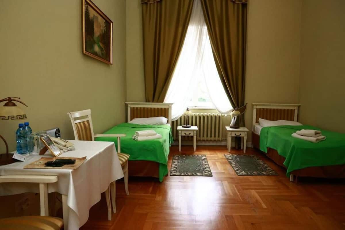 Una stanza con due letti, un tavolo con un telefono e bottiglie d'acqua, e una finestra con tende.