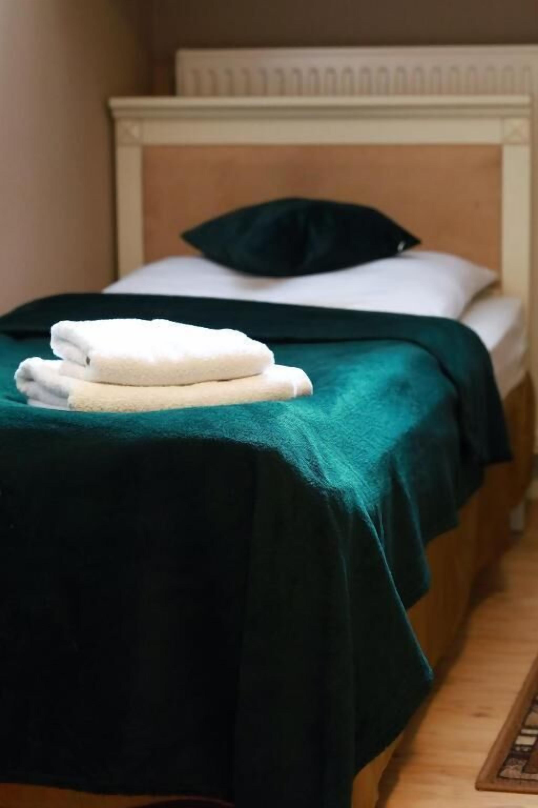 Ein Bett mit grüner Bettdecke, weißen Kissen und gefalteten weißen Handtüchern.