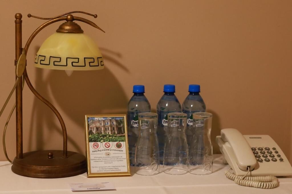 A table with a lamp, water bottles, a framed picture, and a telephone.