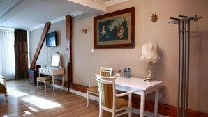 Une chambre d’hôtel équipée d’une table à manger, de chaises, d’un bureau avec un ordinateur, d’une télévision et d’un tableau au mur.