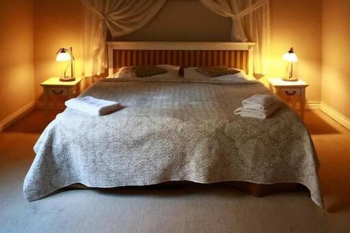 Una camera da letto con un letto, tende, due abat-jour e un comodino.