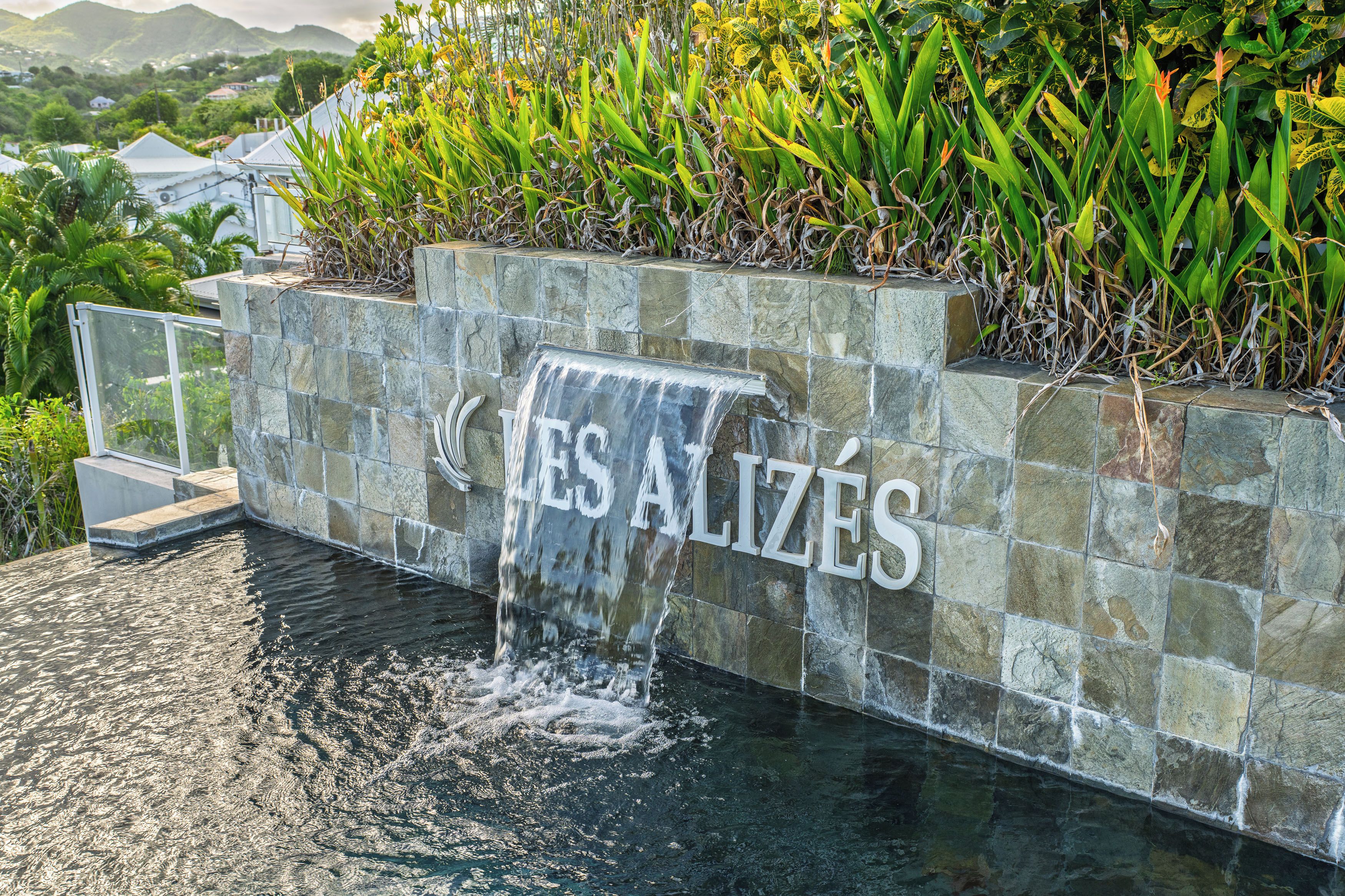 A stone wall with a waterfall feature and the text 'LES ALIZÉS' engraved on it.