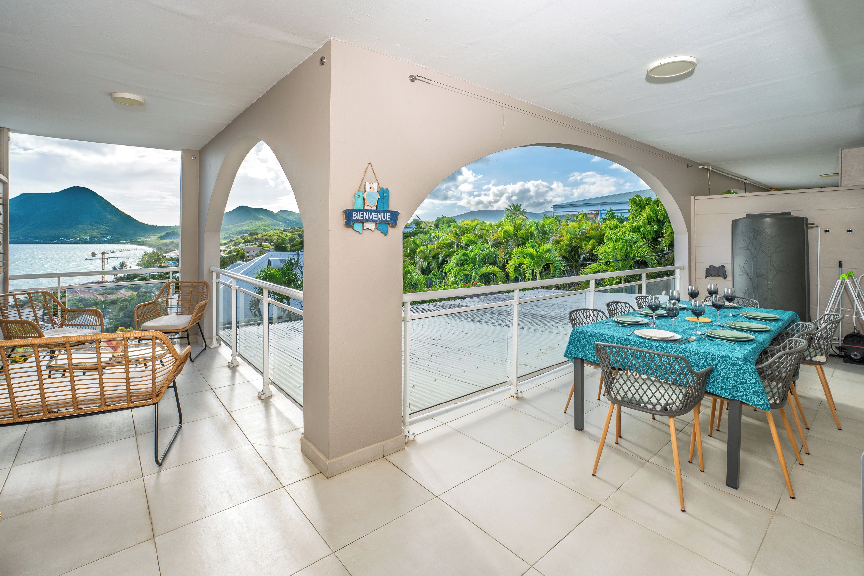 Un balcon avec une table dressée pour le dîner, offrant une vue sur un jardin luxuriant et un paysage montagneux.