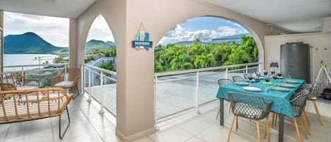 Ein Balkon mit Esstisch, der auf einen üppigen Garten und eine gebirgige Landschaft blickt.