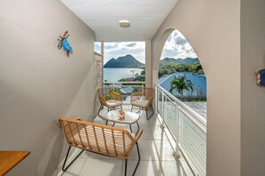 Een balkon met rieten meubilair, uitzicht op een berg en water, en een heldere lucht.
