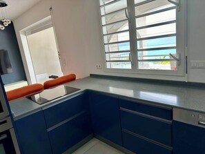 Eine moderne Küche mit blauen Schränken, einem Einbauofen und einem Fenster mit Jalousien.