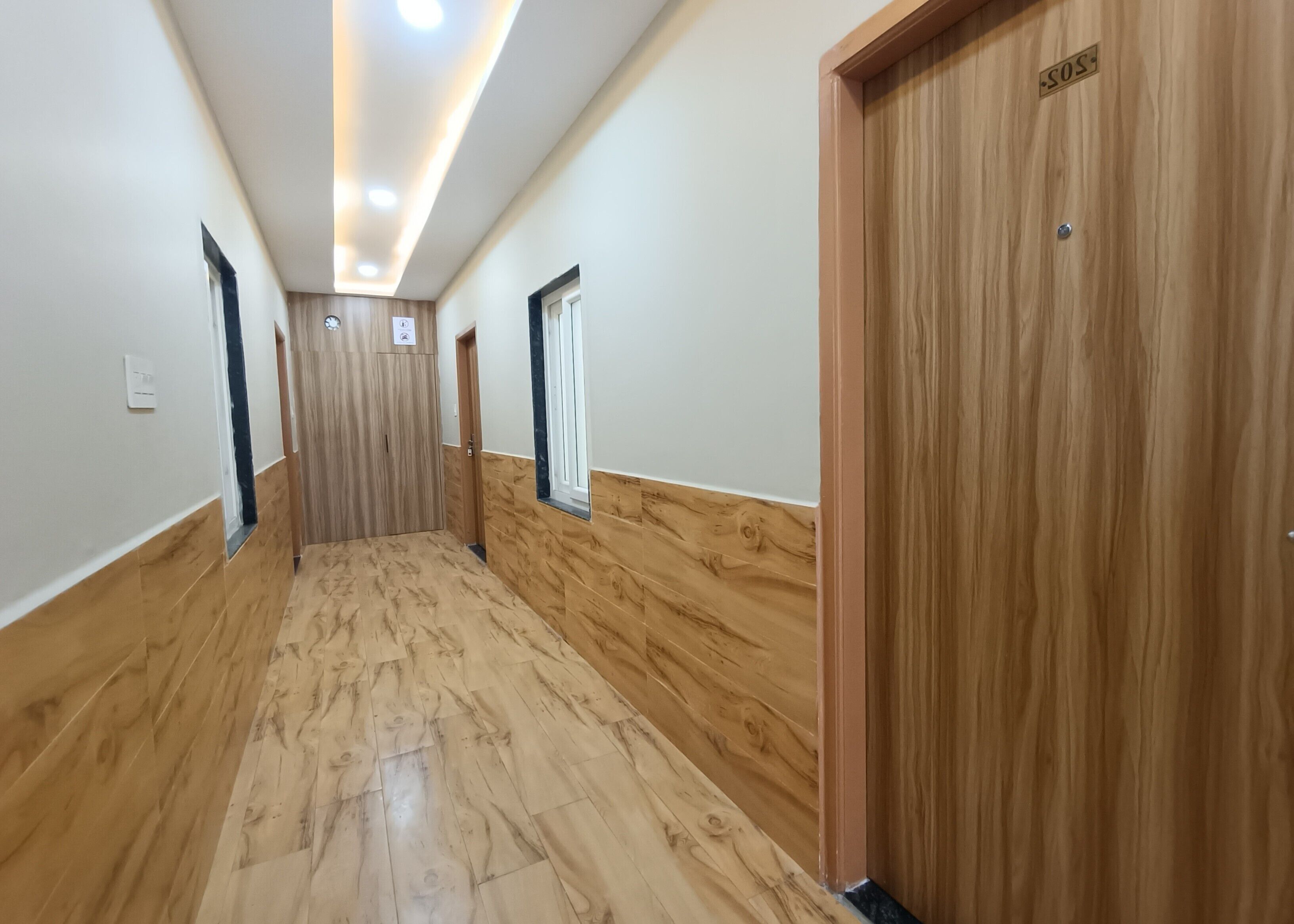 A hallway with wooden flooring, a wooden door labeled 'SOS,' and a window on the right wall.