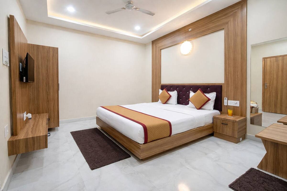 A modern hotel room with a large bed, wooden furniture, a ceiling fan, and a mirror.