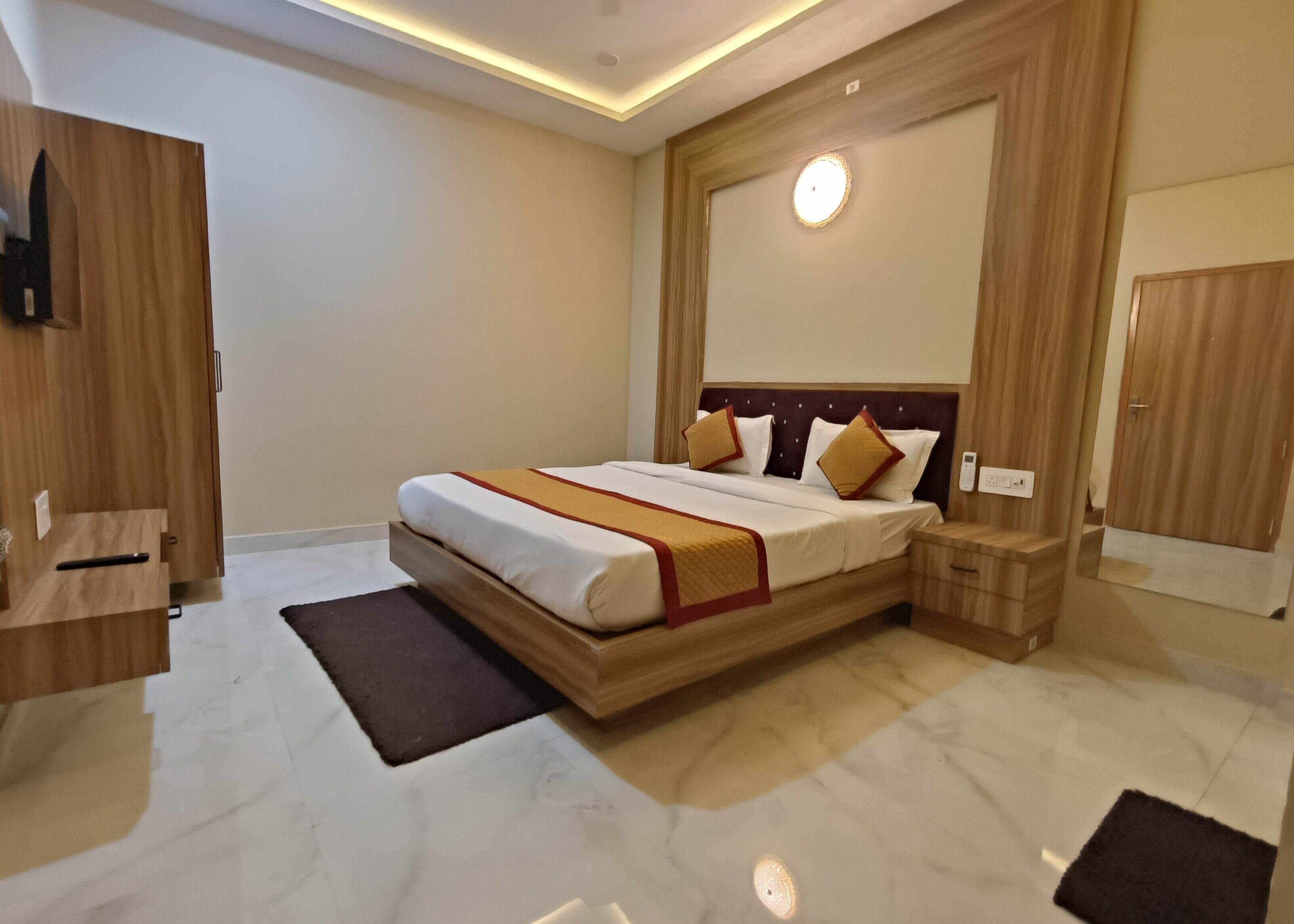 Una habitación de hotel moderna con una cama grande, cabecero de madera, mesitas de noche y un televisor integrado.