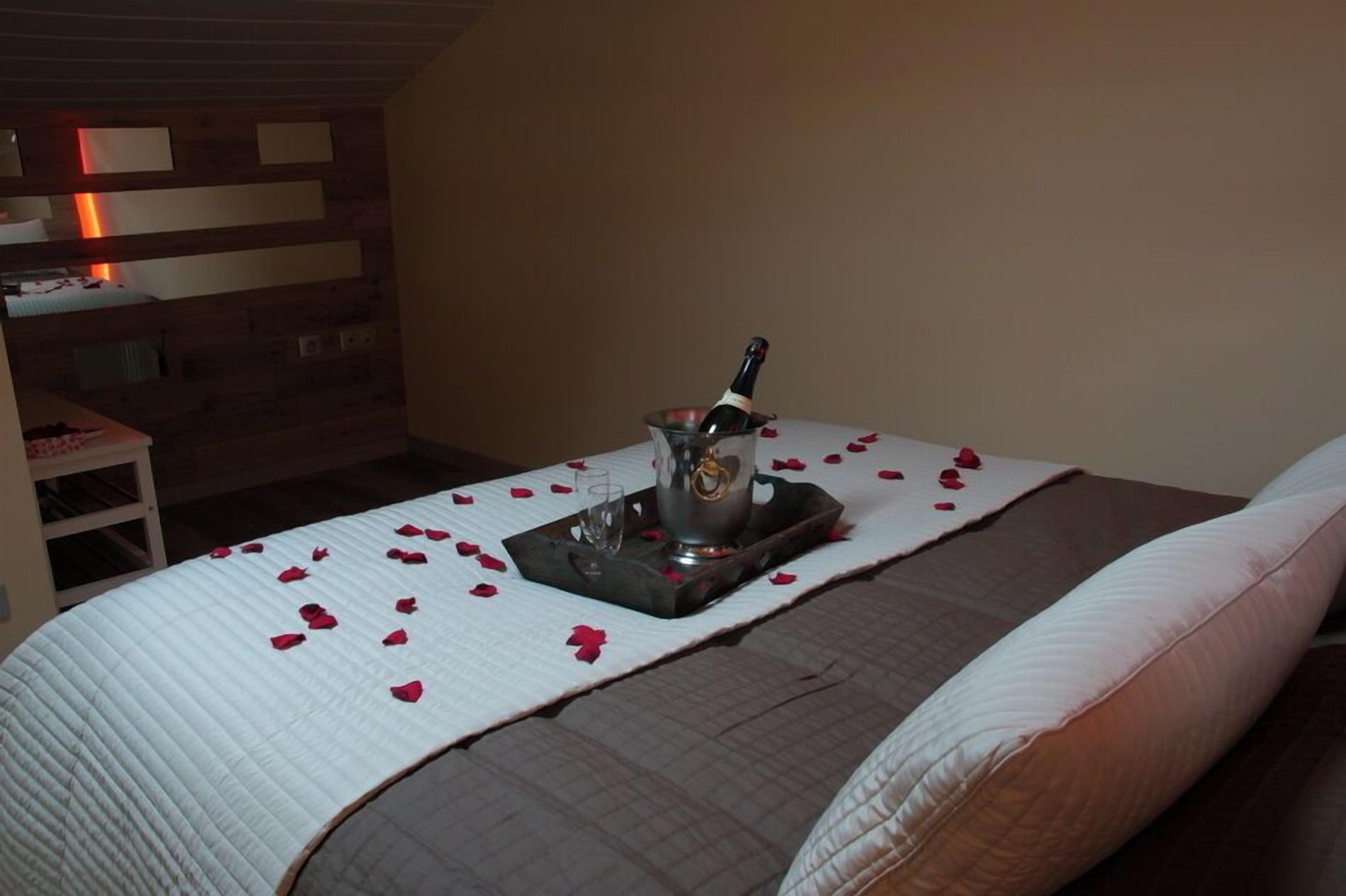 A bed with rose petals, a bottle of champagne, and a tray.