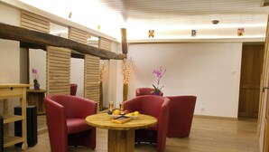 Een kamer met een houten vloer, een ronde houten tafel en rode stoelen. Op de tafel staan twee potplanten.
