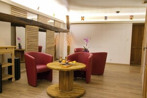 Una habitación con suelo de madera, una mesa redonda de madera y sillas rojas. Hay dos plantas en macetas sobre la mesa.