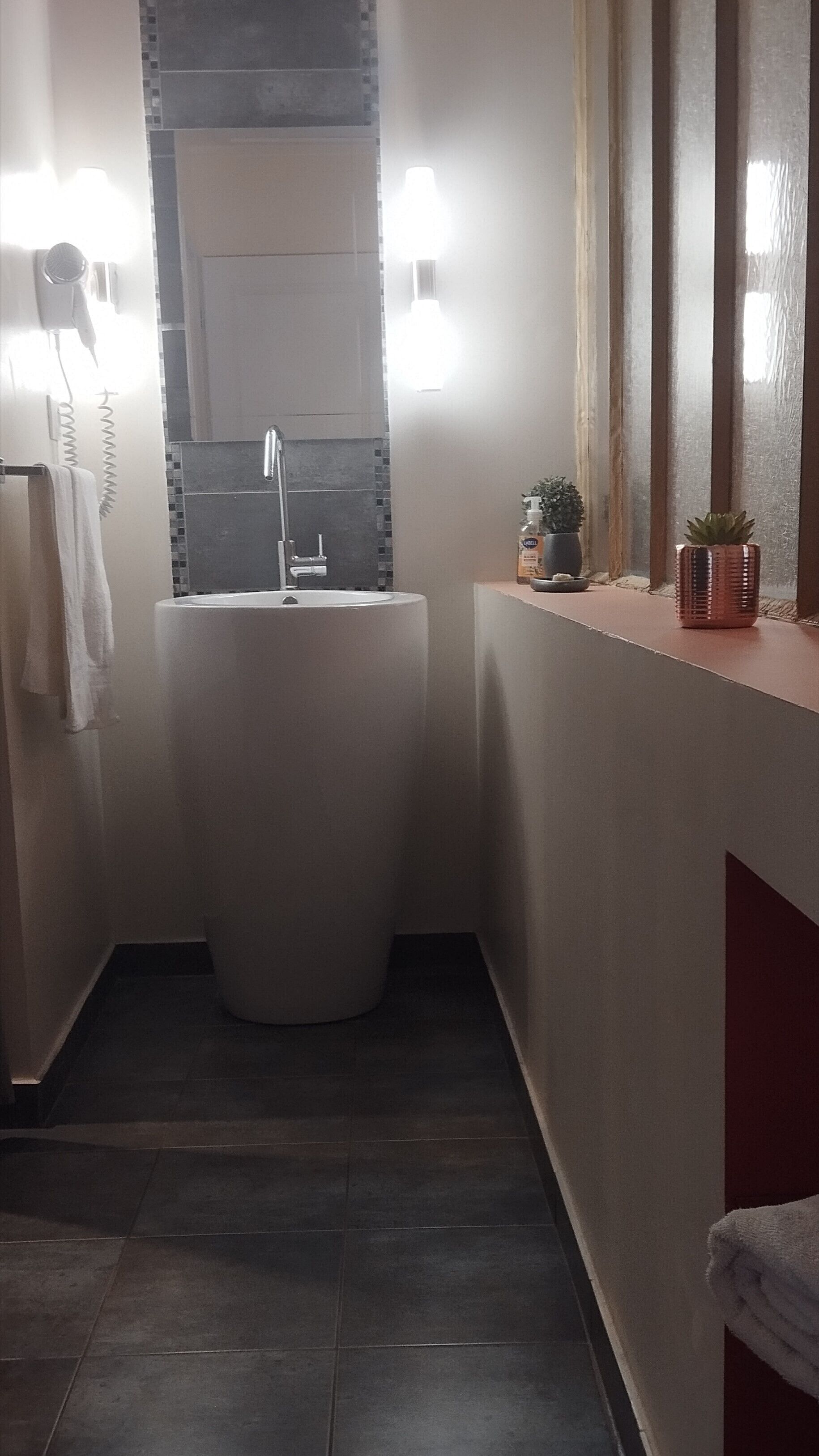 Un baño moderno con un lavamanos independiente, un espejo y una ventana con persianas.