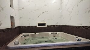 Een whirlpool met bedieningspaneel, omgeven door marmeren wanden en een donkerbruine tegelrand.