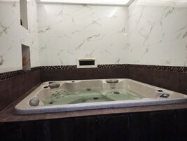 Un jacuzzi con panel de control, rodeado de paredes de mármol y un borde de baldosas marrón oscuro.