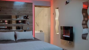 Een moderne slaapkamer met een bed, inbouwschappen, een televisie en een douchehoek.