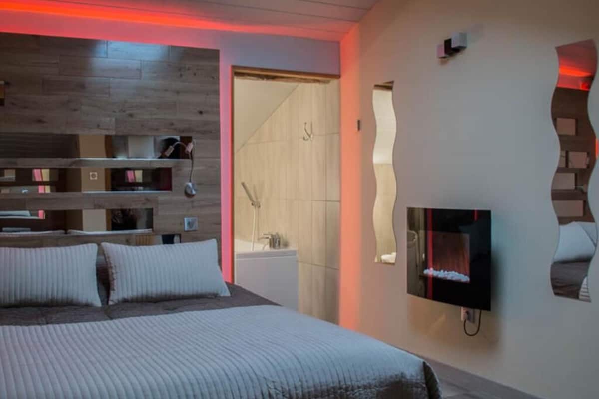 A modern bedroom with a bed, built-in shelving, a TV, and a shower area.