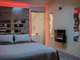 Un dormitorio moderno con cama, estanterías empotradas, televisor y zona de ducha.