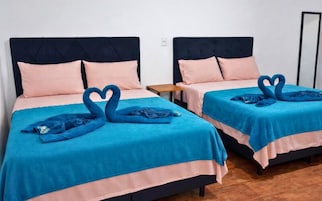 Dos camas individuales con ropa de cama azul y melocotón a juego, situadas en una habitación con suelo de madera y una pequeña mesita de noche entre ellas.