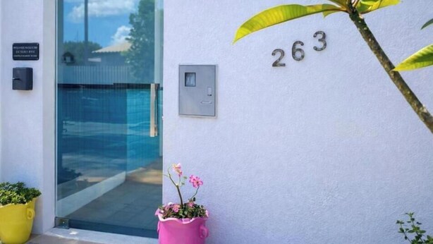 A building entrance with a glass door, a potted plant, and the number 263 on the wall. - Pousada Miss Roses (Foz do Iguaçu)