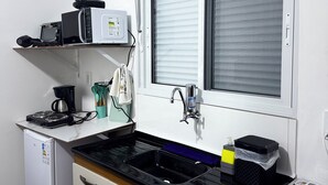A compact kitchen with a refrigerator, stove, microwave, sink, and an air conditioner mounted on the wall. - Pousada Miss Roses (Foz do Iguaçu)