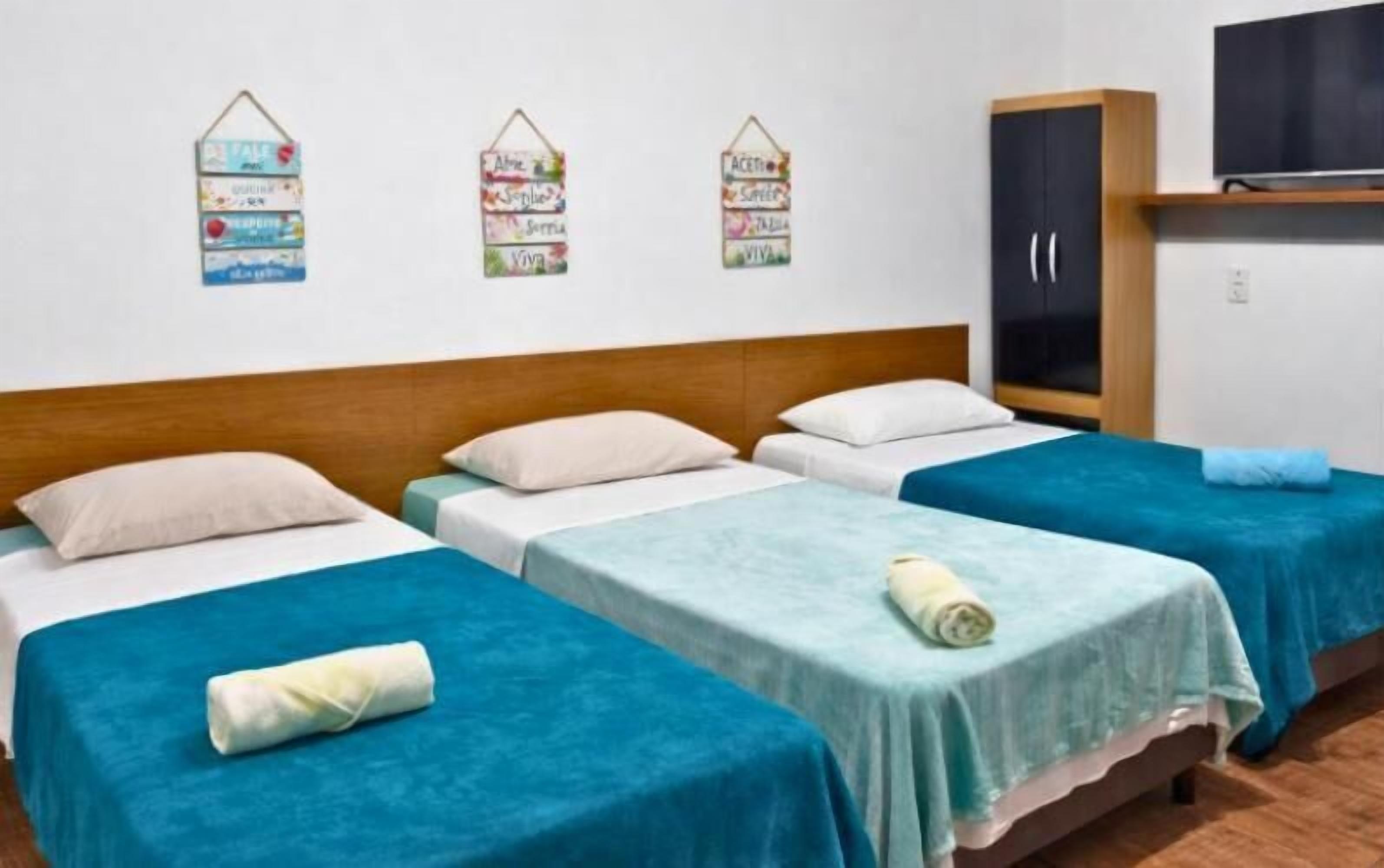 Une chambre d’hôtel avec trois lits simples, une tête de lit en bois, une armoire et des éléments décoratifs sur les murs.
