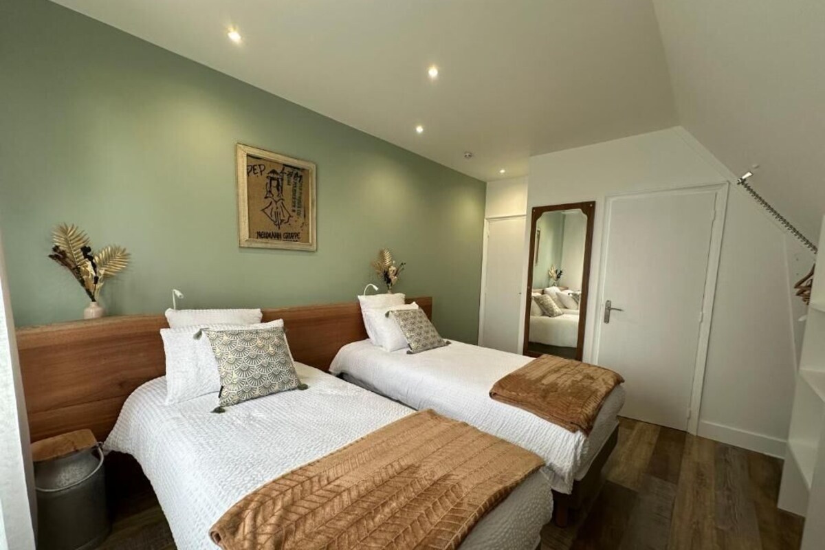 A bedroom with two beds, a mirror, a door, and a framed artwork on the wall.