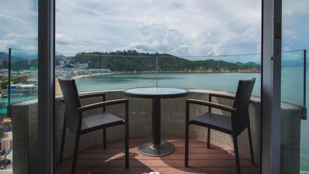 Uma varanda com mesa e cadeiras, com vista para a costa, montanhas e praia.