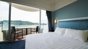 Quarto de hotel com cama, vista para o mar e varanda com cadeiras.
