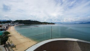 Vista costeira a partir de uma varanda, com praia, mar e montanhas ao longe.