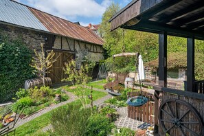 A rustic garden with a wooden fence, a swing, and a stone building with a metal roof. - Small Holiday Home for up to 3 Guests (48 m²) in Udler (Vulkaneifel) (Udler)