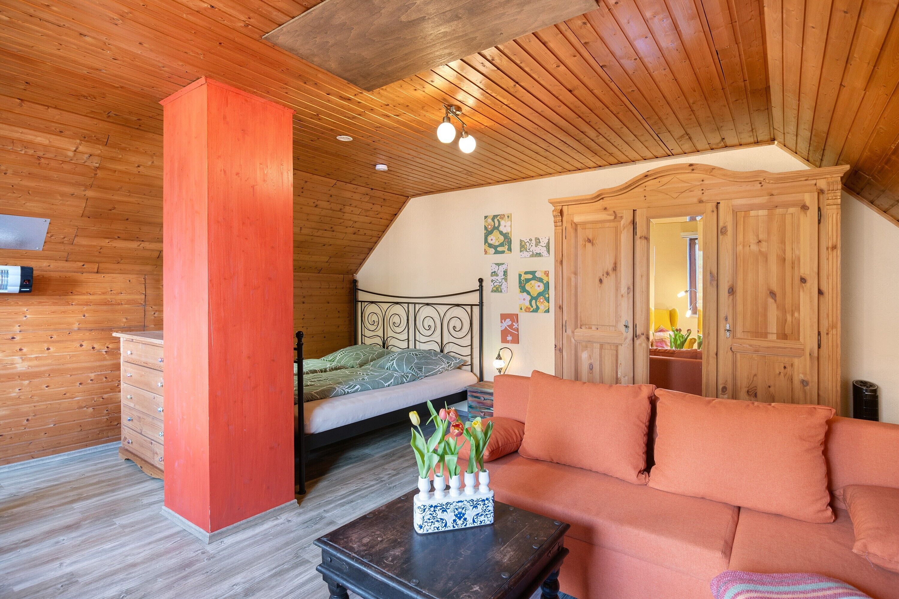 Un dormitorio con techo de madera, una cama, un aparador, un sofá y una mesa con un jarrón de flores.