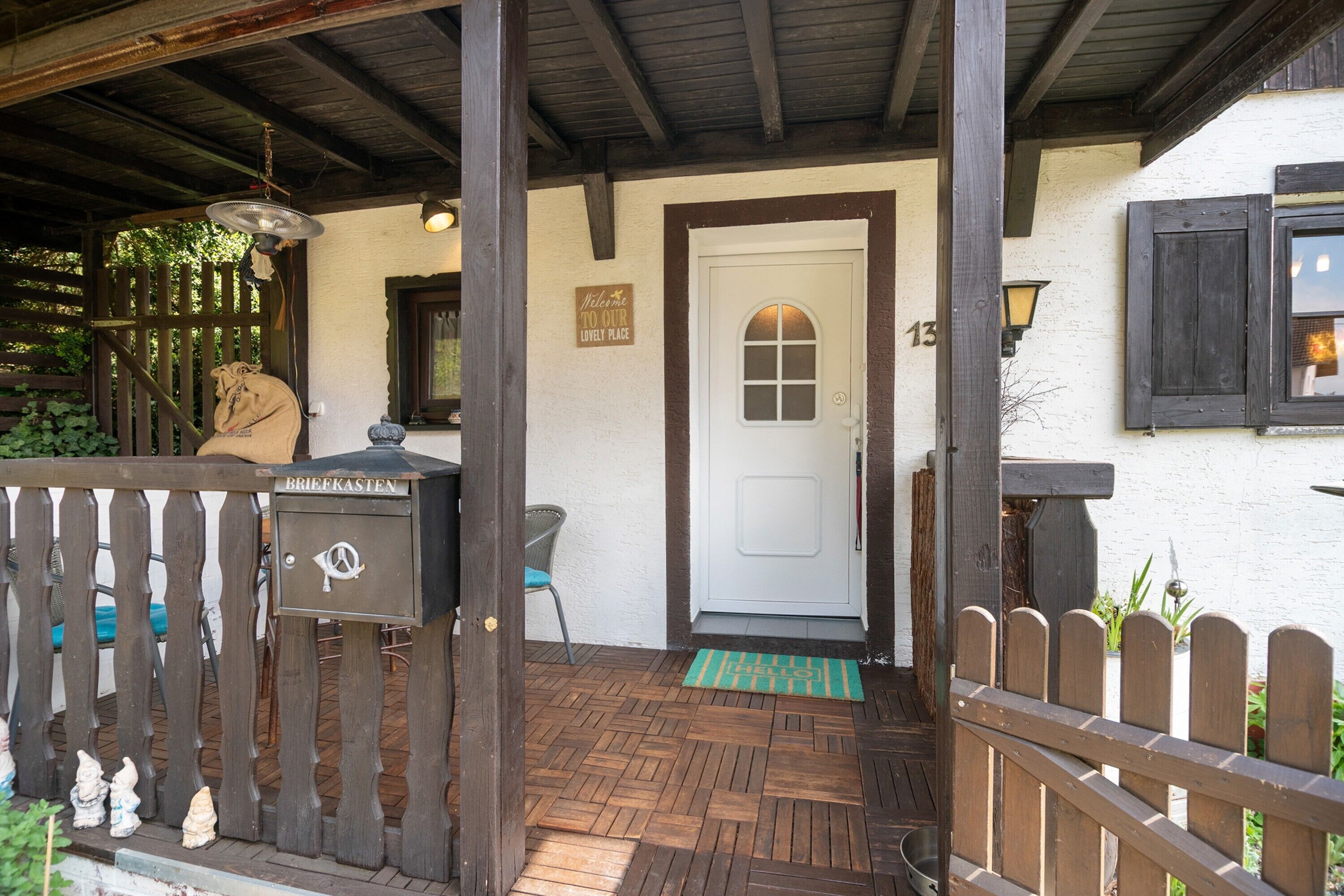 A wooden porch with a mailbox, a door with a number, and a welcome sign.
