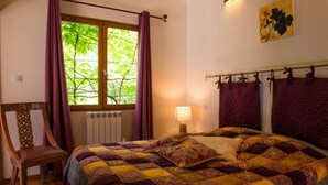 A bedroom with a large bed, a chair, a window with curtains, a radiator, and a wall-mounted lamp. - Chalet Suite Iris (Saint-Remèze)
