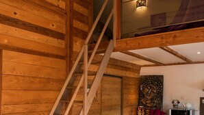 A wooden interior with a dining table, chairs, a staircase, and a kitchen area. - Chalet Suite Iris (Saint-Remèze)