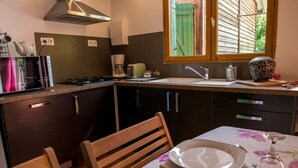 A kitchen with dark cabinets, a gas stove, a coffee maker, and a window with green shutters. - Chalet Suite Iris (Saint-Remèze)