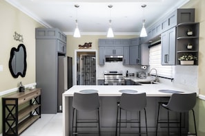 A modern kitchen with grey cabinetry, a central island with bar stools, and pendant lighting. - Clare's Manor in Ocho Rios With Mini Golf Course (Ocho Rios)
