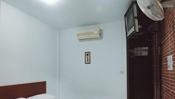 A small, clean room with a single bed, a wall-mounted air conditioner, a TV, and a door leading to a brick exterior. - Orchids Guesthouse (Chiang Rai)