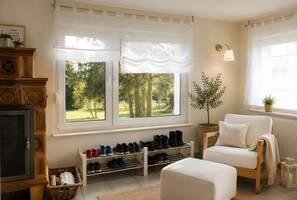Un salon chaleureux avec une cheminée, un porte-chaussures, un fauteuil blanc et une vue sur un parc grâce à de grandes fenêtres.