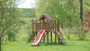 Une structure de jeux en bois, dotée d’un toboggan et d’éléments d’escalade, installée dans un espace herbeux.
