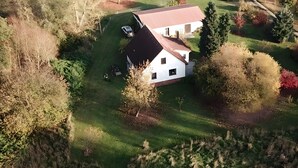 Vue aérienne d’une maison avec un toit en pente, entourée d’une pelouse bien entretenue et d’arbres.