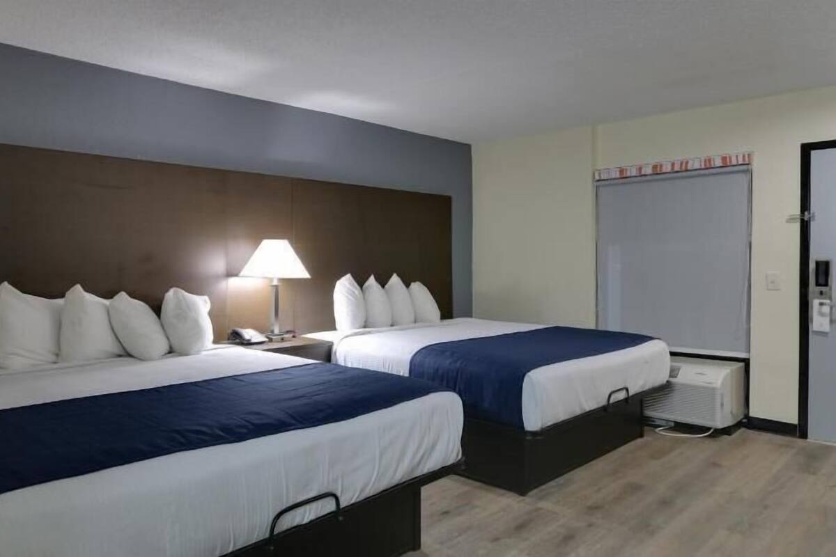 Ein Hotelzimmer mit zwei Betten, einem Nachttisch mit Lampe, einem Kleiderschrank und einem Heizkörper.
