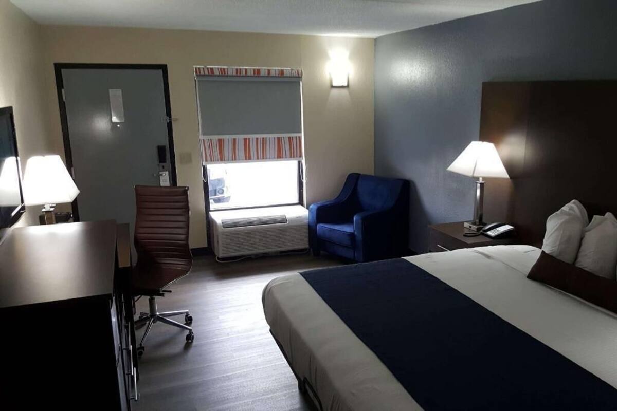 Ein Hotelzimmer mit Bett, Schreibtisch, Stuhl und einem Fenster mit Jalousien.