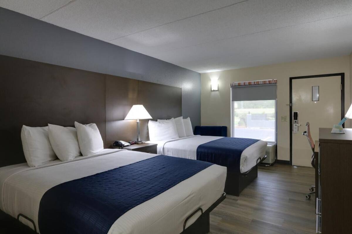 Ein Hotelzimmer mit zwei Betten, einem Schreibtisch, einer Lampe, einem Spiegel und einer Tür.