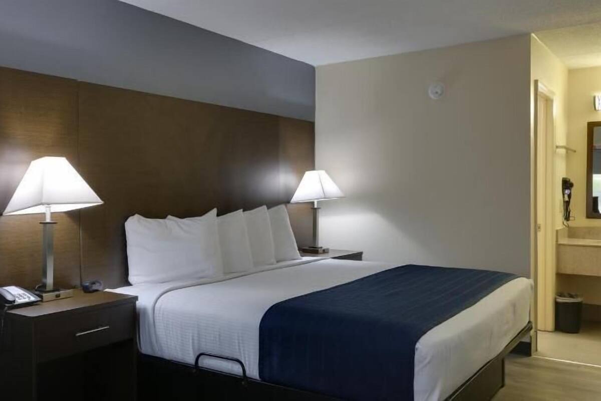 Ein Hotelzimmer mit einem Bett, zwei Nachttischlampen, einem Nachttisch, einem Telefon, einem Spiegel und einem Waschbecken.